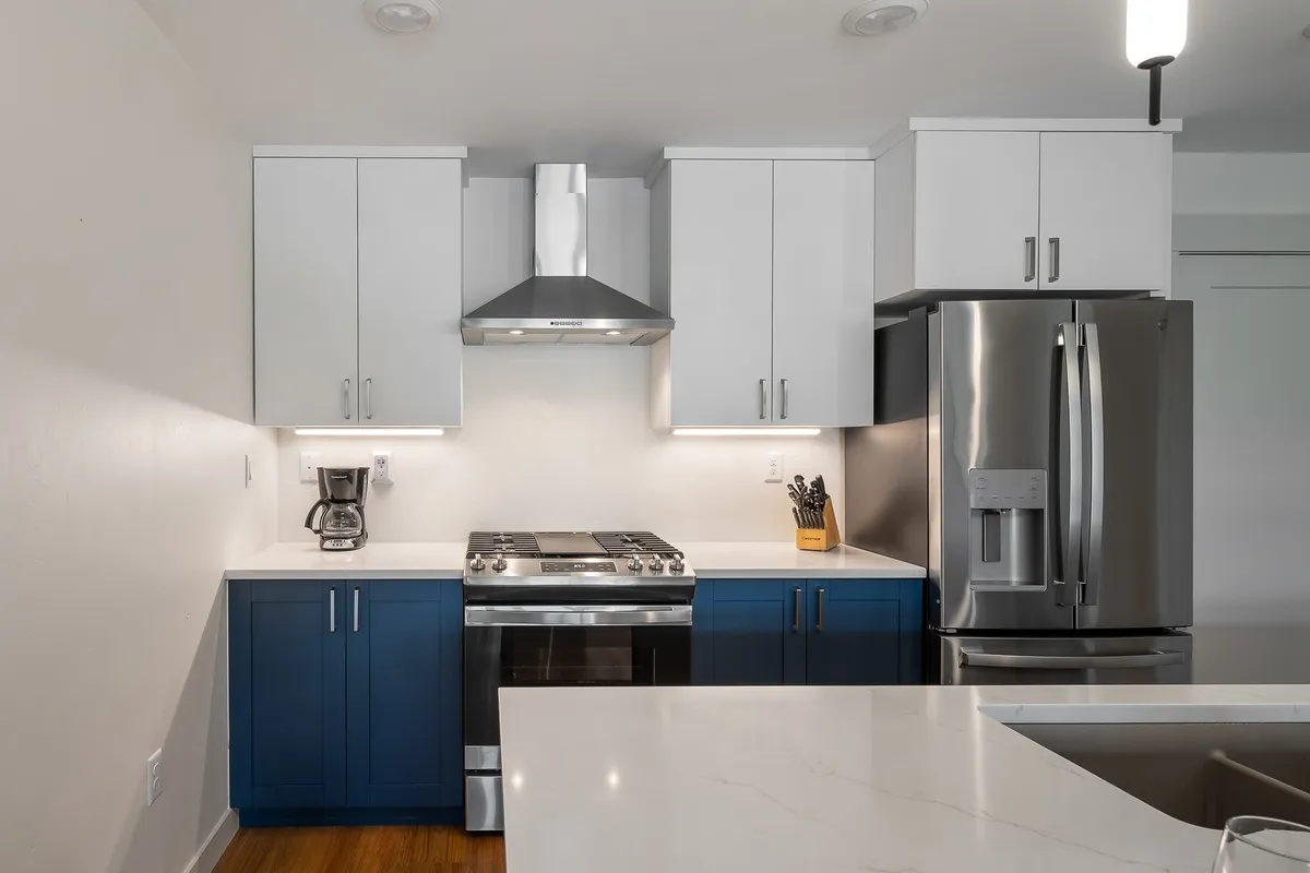A contemporary kitchen with stainless steel appliances, blue cabinetry, white countertops, and a spacious kitchen island. The setup is ideal for cooking, entertaining, and gathering with friends and family, reflecting a modern mountain flair.
