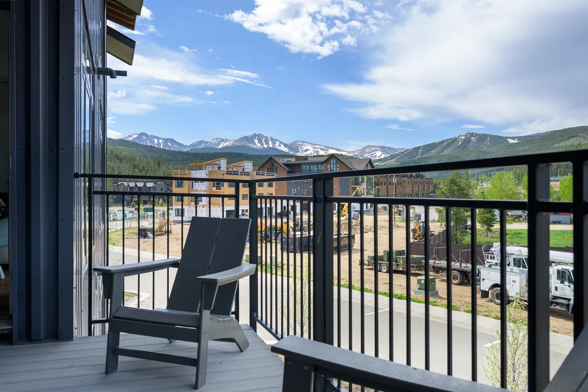 A tranquil balcony scene with comfortable chairs overlooking majestic mountain views and newly constructed buildings. The space invites relaxation, morning coffee, or evening stargazing while enjoying the natural surroundings.