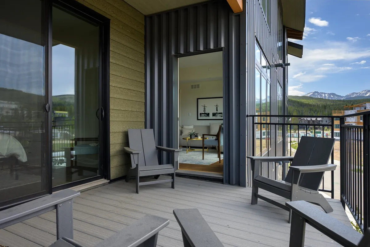 A pair of Adirondack chairs set on a patio, facing an expansive mountain view beyond. The open door hints at seamless indoor-outdoor living, allowing guests to relax with a drink and take in the tranquil scenery from the comfort of their own space.