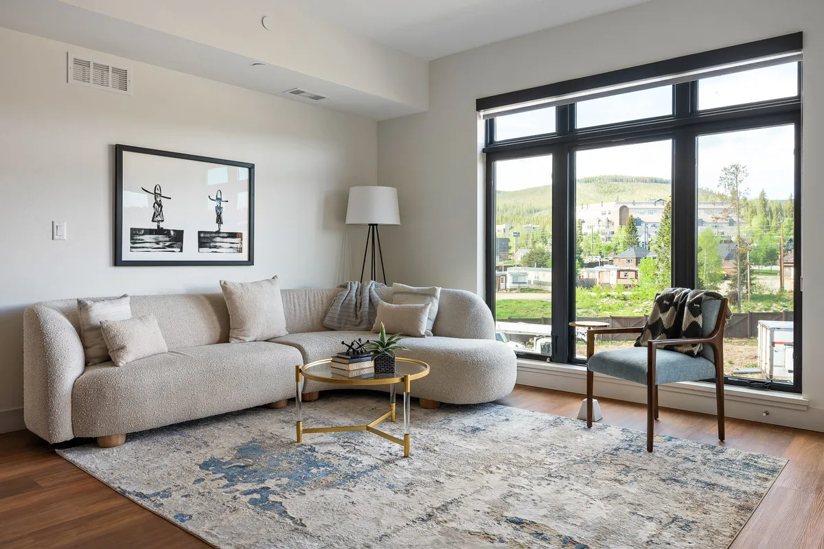 A spacious and inviting living room with a curved sofa oriented toward large windows that fill the space with sunlight. Artful décor and a decorative plant create a relaxing, contemporary atmosphere, ideal for recharging after adventures.