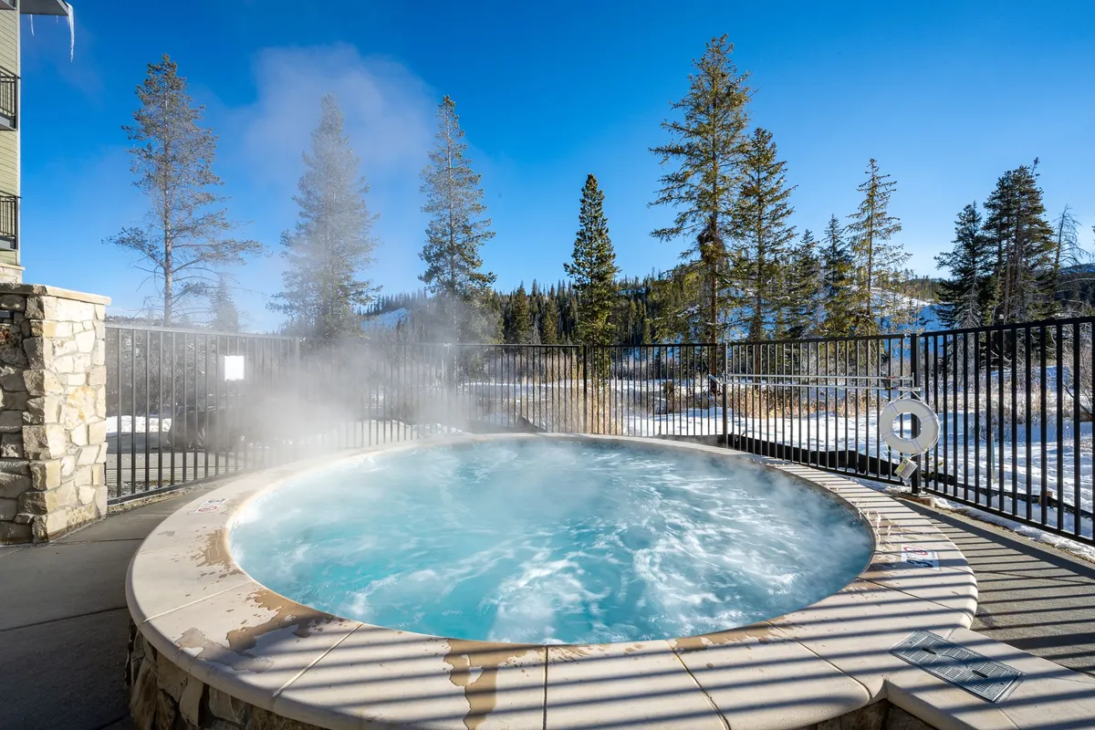 An inviting outdoor hot tub nestled among snow-covered trees, with steam rising from the warm water. The area is surrounded by nature, providing a sense of seclusion and tranquility, perfect for unwinding after a day of mountain adventure.