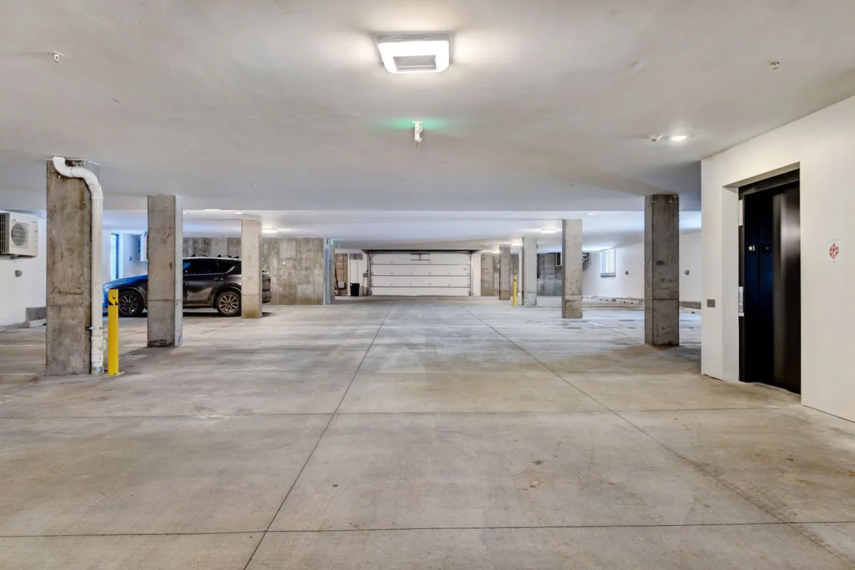 A modern underground parking garage with marked parking spaces, concrete pillars, and an elevator providing direct access to the living areas. The environment is clean, well-lit, and secure, underscoring the convenience for residents and guests alike.