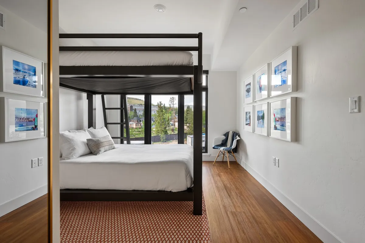 A bright, comfortable bunk bed room with large windows that let in natural light. The space is accented with colorful artwork and offers a cozy spot for children or extra guests to relax, read, or gaze outside at the surrounding scenery.